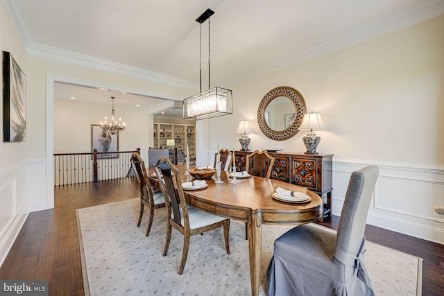 dining room featuring a notable chandelier, crown molding, dark wood-type flooring, a decorative wall, and wainscoting