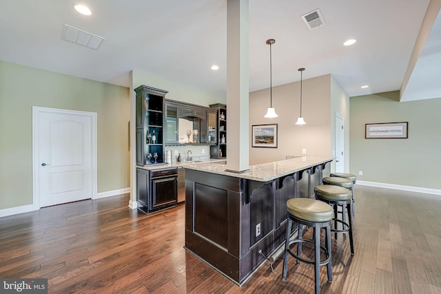 kitchen with a sink, light stone counters, a breakfast bar area, dark wood-type flooring, and visible vents