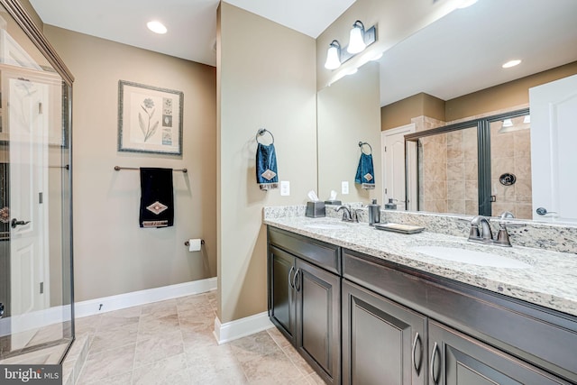 full bathroom with a stall shower, baseboards, double vanity, and a sink