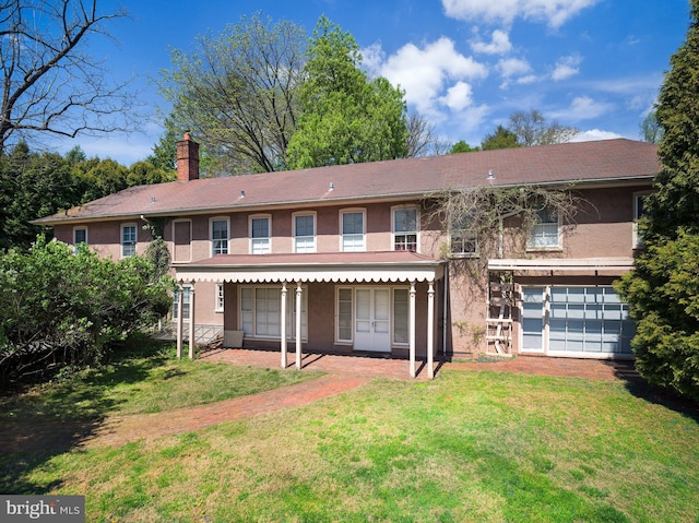 rear view of house with stucco siding, a chimney, and a lawn