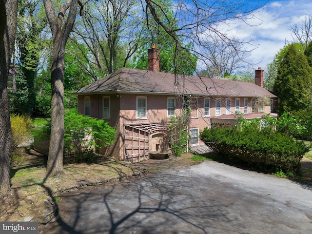 rear view of house with a shingled roof, stucco siding, and a chimney