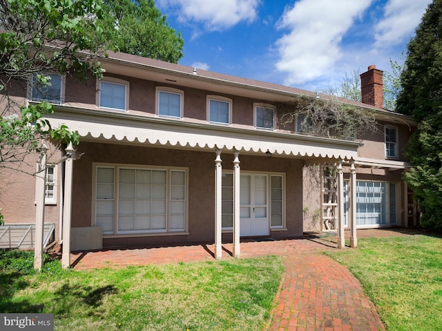 back of property featuring a chimney, stucco siding, and a lawn