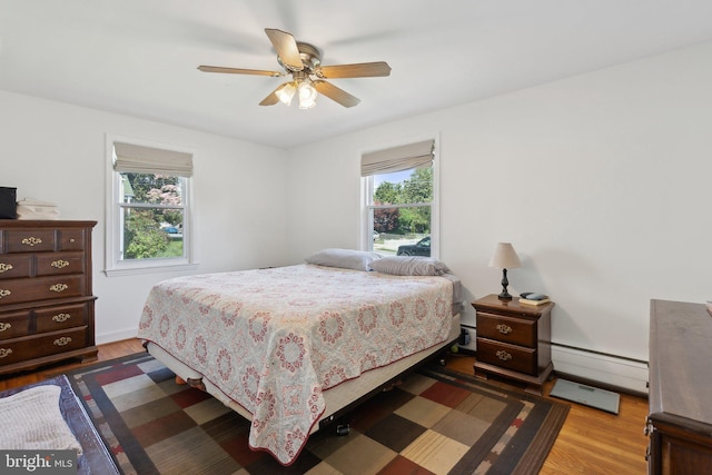 bedroom featuring multiple windows, a baseboard heating unit, and wood finished floors