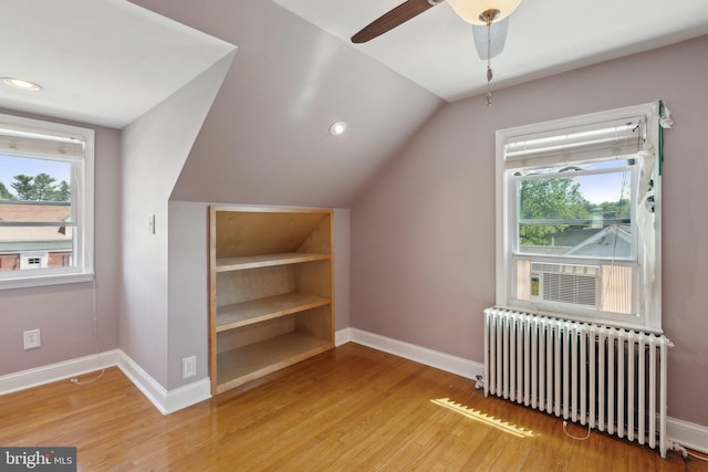 additional living space with baseboards, plenty of natural light, wood finished floors, and radiator