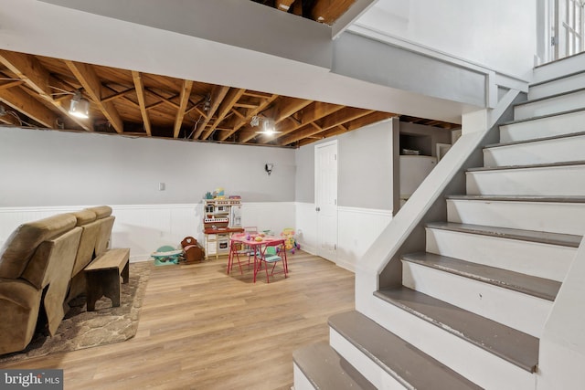 finished below grade area with a wainscoted wall, stairs, and wood finished floors