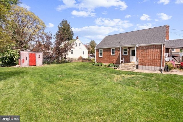 rear view of house featuring fence, a shed, brick siding, a lawn, and an outbuilding