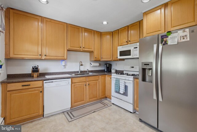 kitchen featuring white appliances, recessed lighting, dark countertops, and a sink