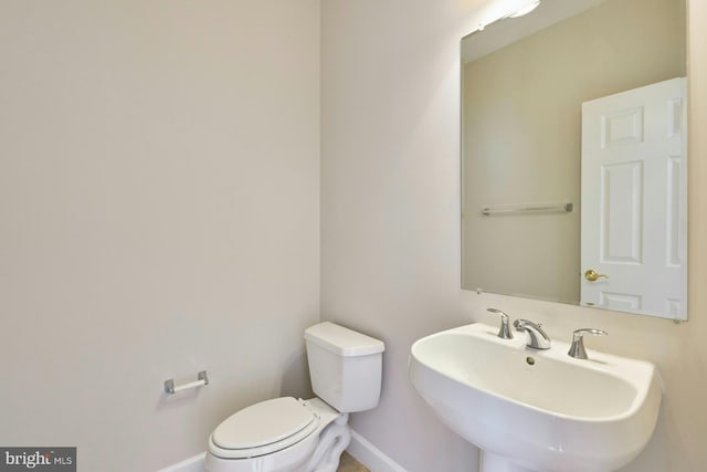 half bathroom featuring toilet, baseboards, and a sink