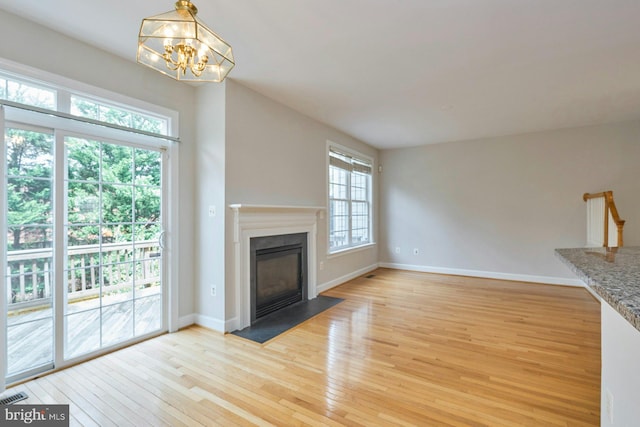 unfurnished living room featuring light wood-style floors, a fireplace with flush hearth, baseboards, and a chandelier