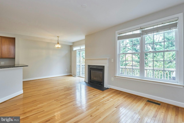 unfurnished living room with a notable chandelier, light wood finished floors, baseboards, a fireplace with flush hearth, and visible vents