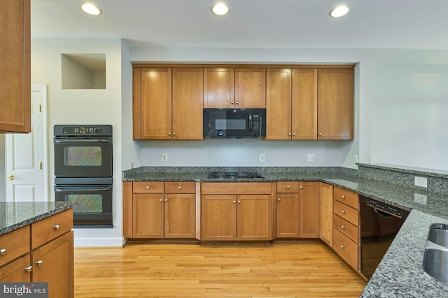 kitchen with brown cabinets, black appliances, light wood-style floors, dark stone counters, and recessed lighting