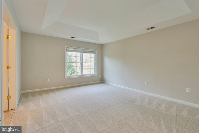 empty room with baseboards, visible vents, a tray ceiling, and light colored carpet