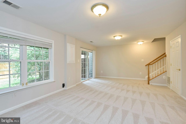 spare room with stairway, baseboards, light colored carpet, and visible vents