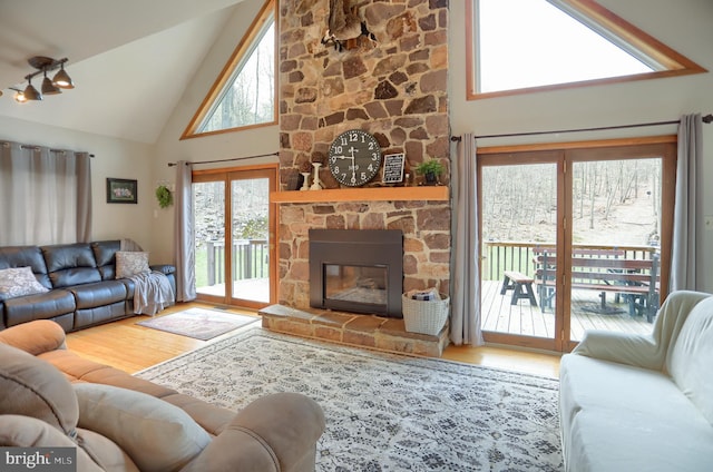 living room with high vaulted ceiling, a stone fireplace, and wood finished floors