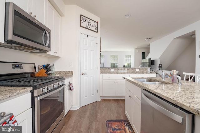kitchen featuring appliances with stainless steel finishes, wood finished floors, a sink, light stone counters, and white cabinetry