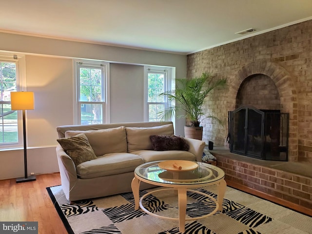 living area featuring crown molding, a brick fireplace, wood finished floors, and visible vents