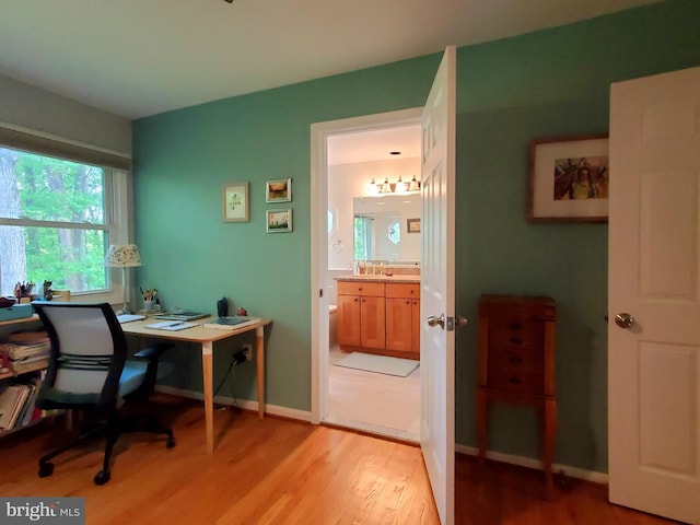 office space featuring a sink, baseboards, and light wood-style flooring
