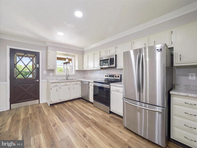 kitchen featuring crown molding, light wood-type flooring, a sink, stainless steel appliances, and white cabinetry