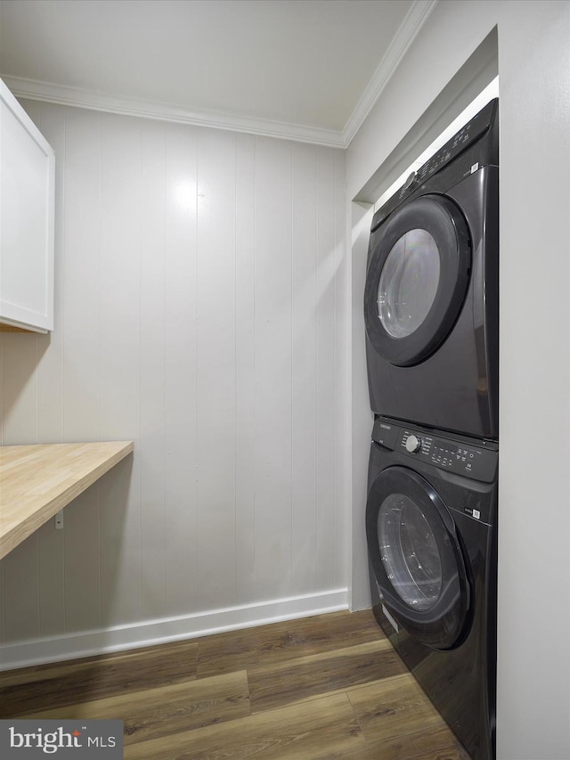 clothes washing area featuring crown molding, stacked washer and dryer, laundry area, wood finished floors, and baseboards