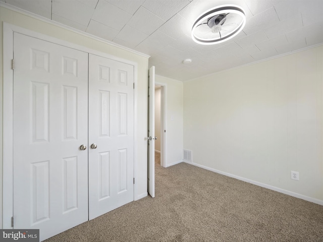 unfurnished bedroom featuring carpet flooring, baseboards, visible vents, ornamental molding, and a closet
