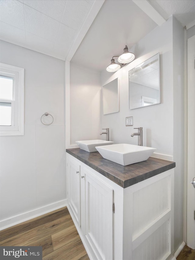bathroom featuring a sink, baseboards, double vanity, and wood finished floors