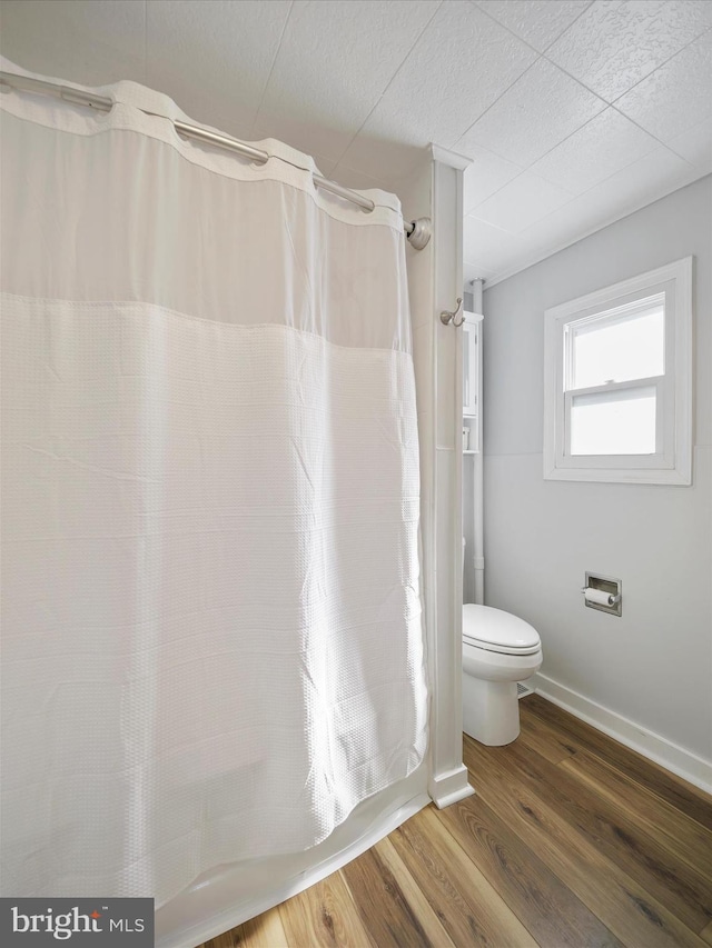 bathroom with baseboards, a shower with curtain, toilet, and wood finished floors