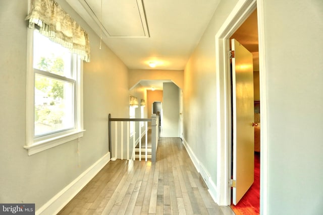 corridor featuring baseboards, attic access, wood finished floors, and an upstairs landing
