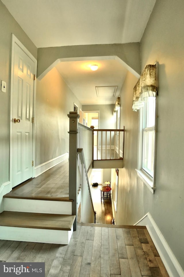 staircase featuring baseboards, attic access, wood finished floors, and a wealth of natural light