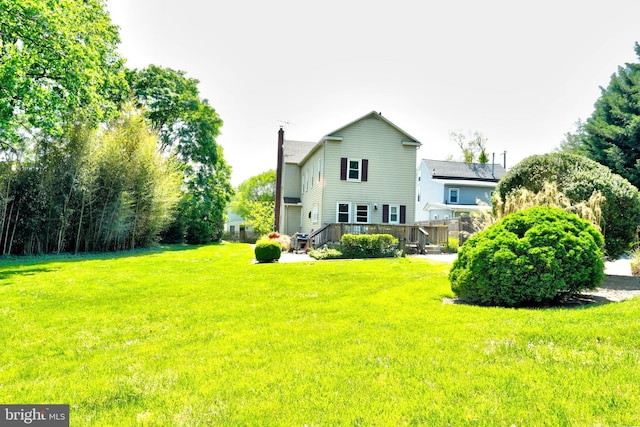 rear view of house with a chimney, a yard, and a deck