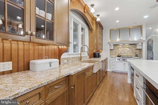 kitchen featuring a sink, light wood-style floors, glass insert cabinets, tasteful backsplash, and light stone counters