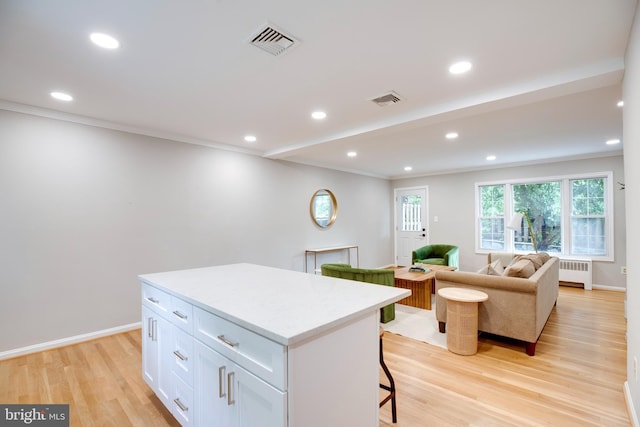 3306 Landover St, Alexandria, VA 22305 - kitchen featuring radiator heating unit, a kitchen breakfast bar, light wood-type flooring, a kitchen island, and white cabinetry