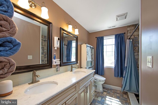 bathroom with tasteful backsplash, stone finish floor, a sink, and visible vents