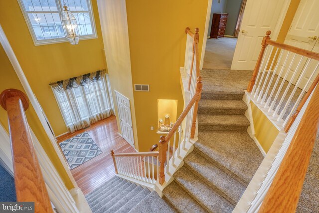 staircase with a chandelier, carpet floors, visible vents, a towering ceiling, and wood finished floors
