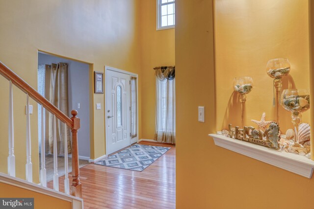entrance foyer featuring wood-type flooring, baseboards, a towering ceiling, and stairs