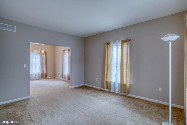 carpeted spare room with baseboards, visible vents, and an inviting chandelier