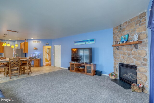 living room with light colored carpet, visible vents, a stone fireplace, and baseboards