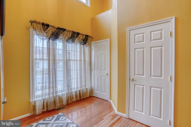 unfurnished bedroom with light wood-style flooring, visible vents, baseboards, and a high ceiling