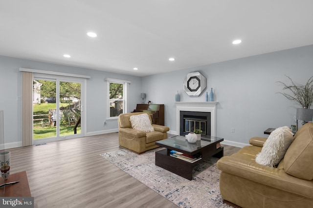 living room featuring a glass covered fireplace, baseboards, recessed lighting, and wood finished floors