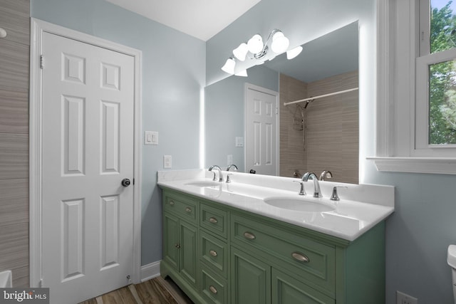 bathroom featuring double vanity, a sink, wood finished floors, and a shower