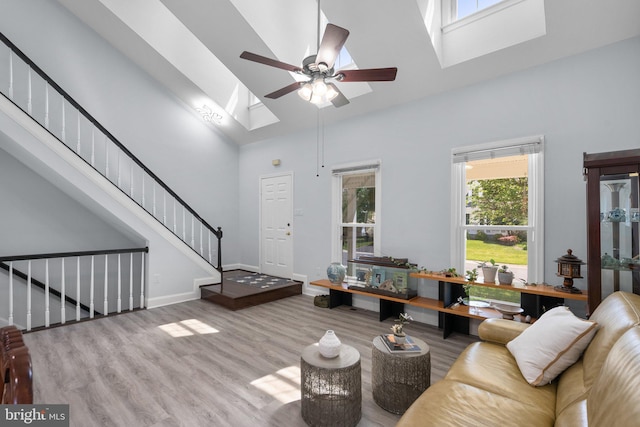 living area with a ceiling fan, a skylight, wood finished floors, stairway, and high vaulted ceiling