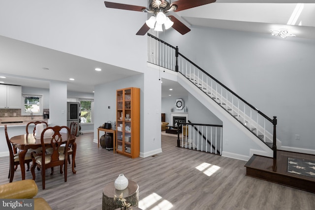living area featuring baseboards, a ceiling fan, a high ceiling, and light wood-style flooring