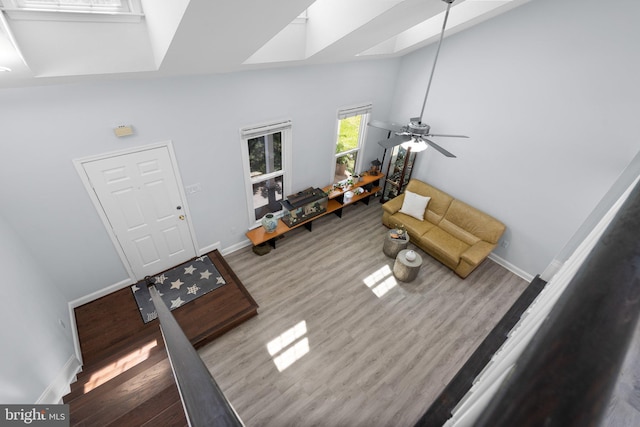 living area featuring baseboards, a skylight, a high ceiling, and wood finished floors