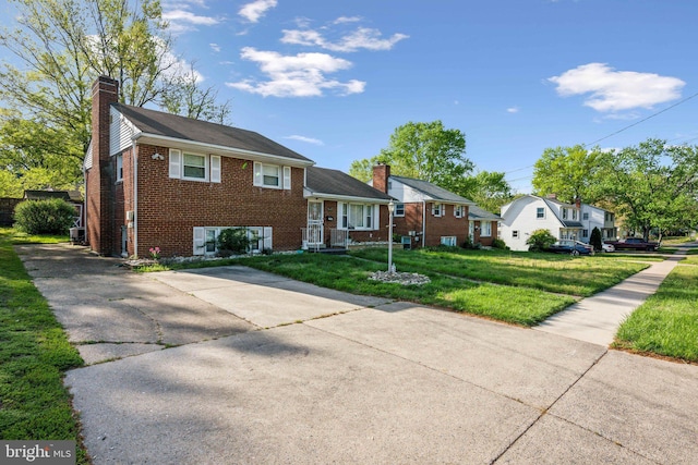 split level home featuring a chimney, brick siding, and a front yard