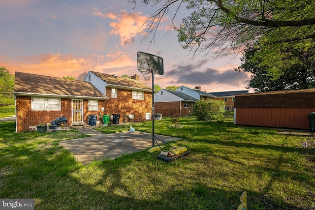 back of house at dusk featuring an outbuilding, brick siding, and a yard