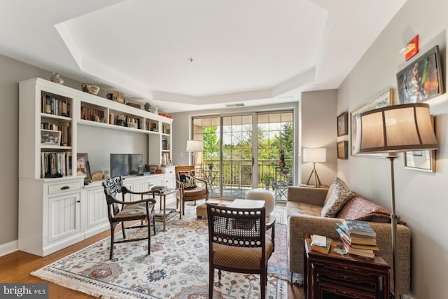 living area with visible vents, wood finished floors, and a raised ceiling