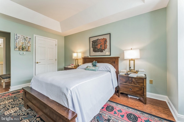 bedroom featuring a tray ceiling, wood finished floors, and baseboards