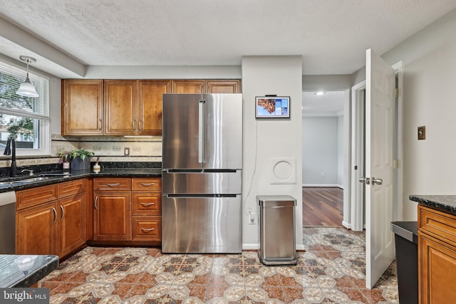 7112 Bonniemill Ln, Springfield, VA 22150 - kitchen featuring freestanding refrigerator, brown cabinets, a sink, dark stone countertops, and hanging light fixtures