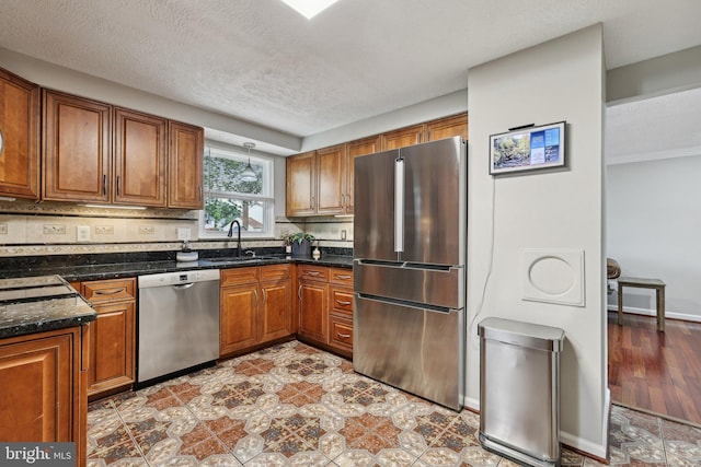 7112 Bonniemill Ln, Springfield, VA 22150 - kitchen featuring appliances with stainless steel finishes, a sink, brown cabinets, decorative backsplash, and a textured ceiling
