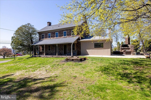 back of property with a lawn, covered porch, a chimney, and a fireplace