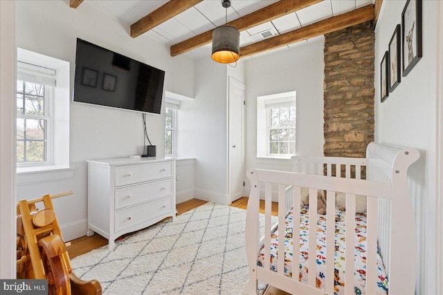 bedroom featuring visible vents, light wood finished floors, beamed ceiling, and multiple windows